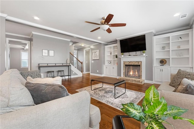 living area with a brick fireplace, stairs, crown molding, and wood finished floors