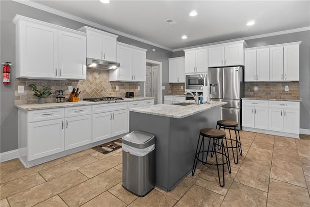 kitchen featuring ornamental molding, an island with sink, under cabinet range hood, appliances with stainless steel finishes, and white cabinets