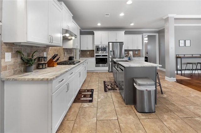 kitchen with ornamental molding, under cabinet range hood, backsplash, white cabinetry, and appliances with stainless steel finishes