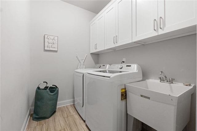 clothes washing area with baseboards, cabinet space, a sink, washing machine and dryer, and light wood-type flooring