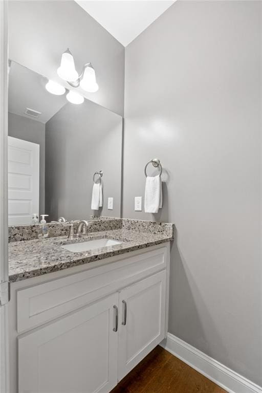 bathroom with visible vents, vanity, baseboards, and wood finished floors