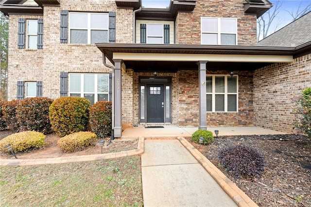 doorway to property featuring a porch and brick siding