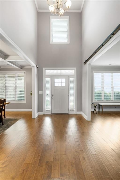 foyer featuring hardwood / wood-style floors, crown molding, baseboards, and an inviting chandelier