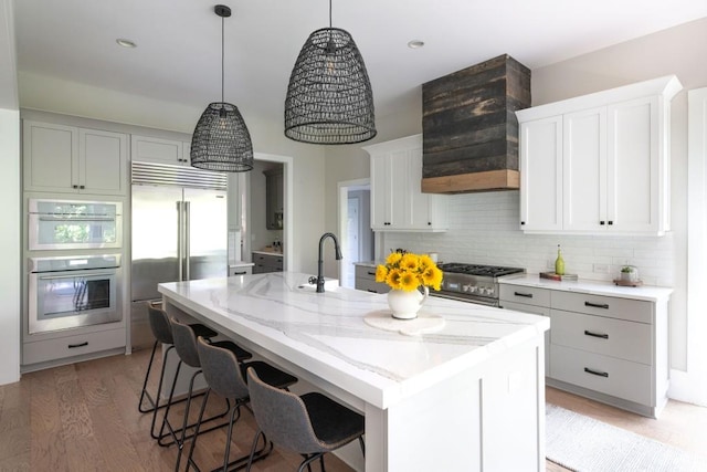 kitchen featuring tasteful backsplash, dark hardwood / wood-style flooring, premium appliances, a kitchen island with sink, and light stone counters