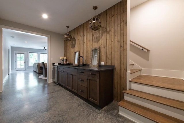 bar featuring wooden walls, decorative light fixtures, sink, dark brown cabinetry, and an inviting chandelier