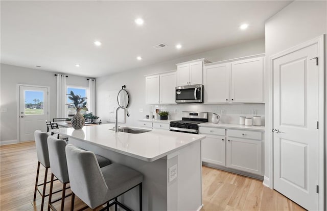 kitchen featuring white cabinets, stainless steel appliances, an island with sink, sink, and light wood-type flooring