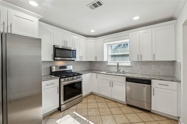 kitchen with sink, white cabinetry, stainless steel appliances, light stone countertops, and decorative backsplash