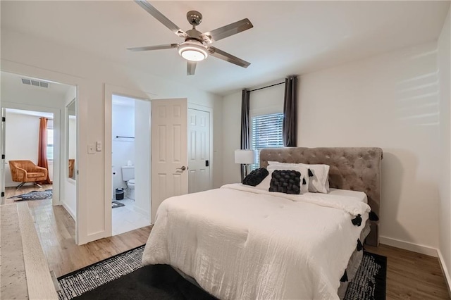 bedroom featuring ceiling fan, ensuite bathroom, visible vents, baseboards, and light wood finished floors