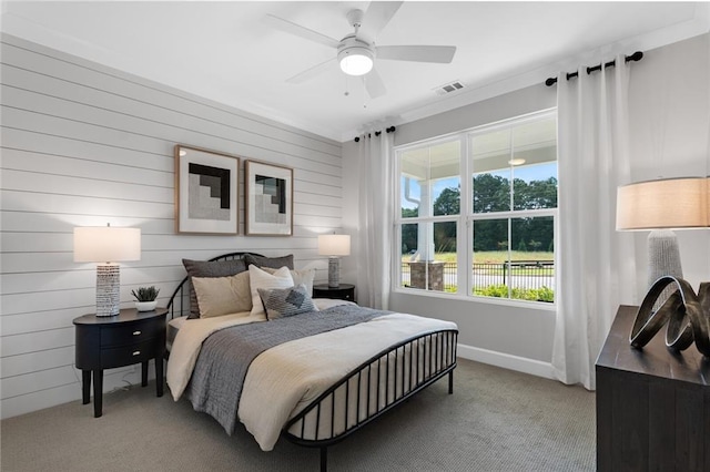 carpeted bedroom featuring ornamental molding, wooden walls, and ceiling fan