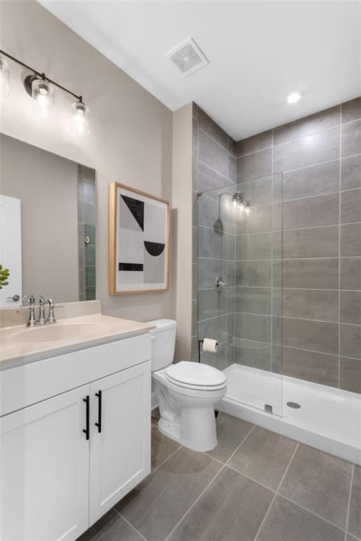 bathroom featuring toilet, tile patterned flooring, vanity, and a tile shower