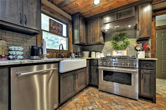 kitchen featuring decorative backsplash, light stone counters, appliances with stainless steel finishes, brick floor, and under cabinet range hood