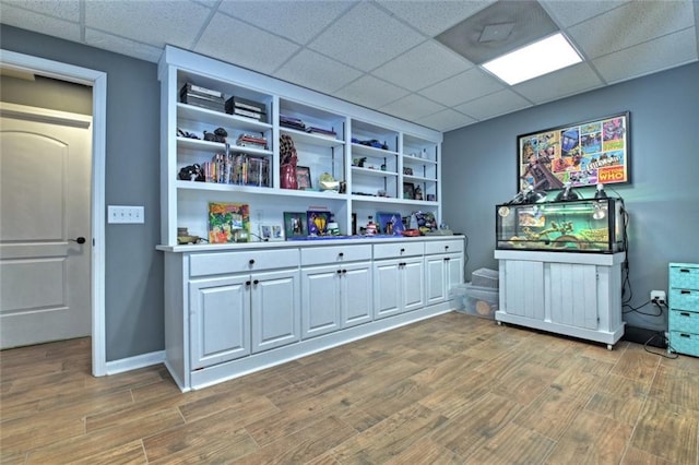 interior space featuring a drop ceiling, baseboards, and wood finished floors