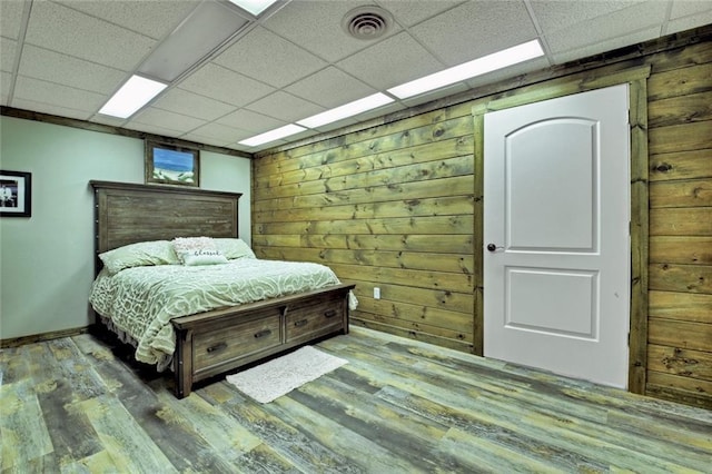 bedroom with a paneled ceiling, wood walls, wood finished floors, and visible vents