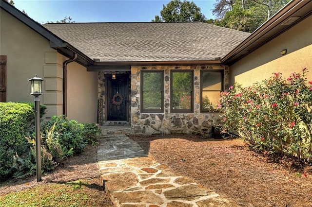 entrance to property with stone siding, a shingled roof, and stucco siding