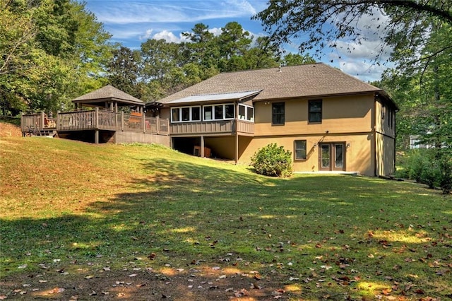 back of house with a yard, stucco siding, a sunroom, and a wooden deck