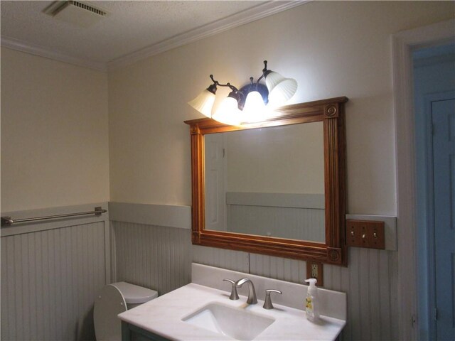 bathroom featuring vanity, visible vents, a wainscoted wall, ornamental molding, and toilet