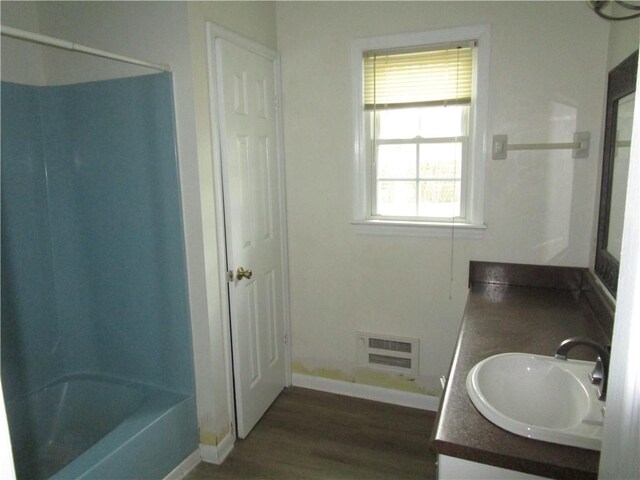bathroom with visible vents, baseboards, double vanity, wood finished floors, and a sink