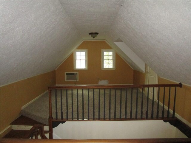 additional living space with a textured ceiling, a wall mounted AC, and lofted ceiling