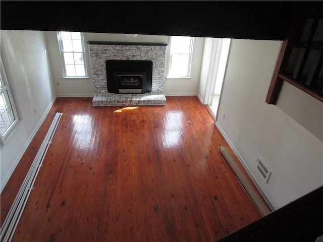 unfurnished living room with visible vents, baseboards, a fireplace, wood-type flooring, and a baseboard radiator