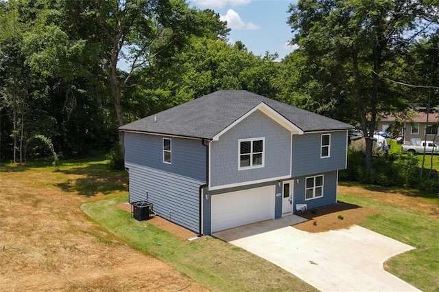 exterior space with a front lawn, cooling unit, concrete driveway, an attached garage, and a shingled roof