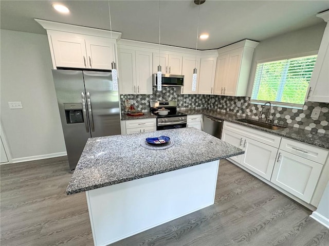 kitchen featuring stainless steel appliances, light wood-style floors, a sink, and dark stone countertops