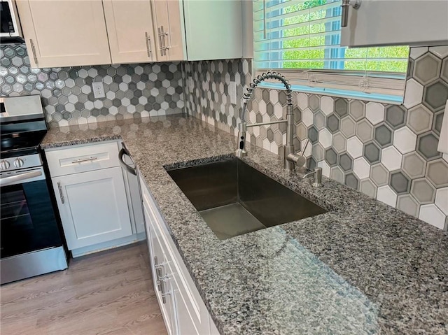 kitchen with tasteful backsplash, a sink, stainless steel range with electric stovetop, light wood-style floors, and white cabinetry