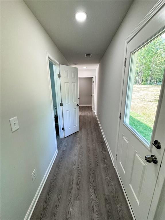 hallway with dark wood finished floors, baseboards, a healthy amount of sunlight, and visible vents