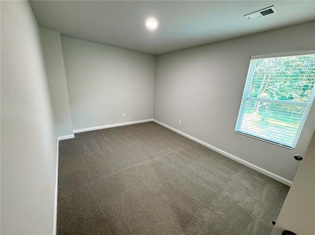 empty room with baseboards, dark colored carpet, and visible vents