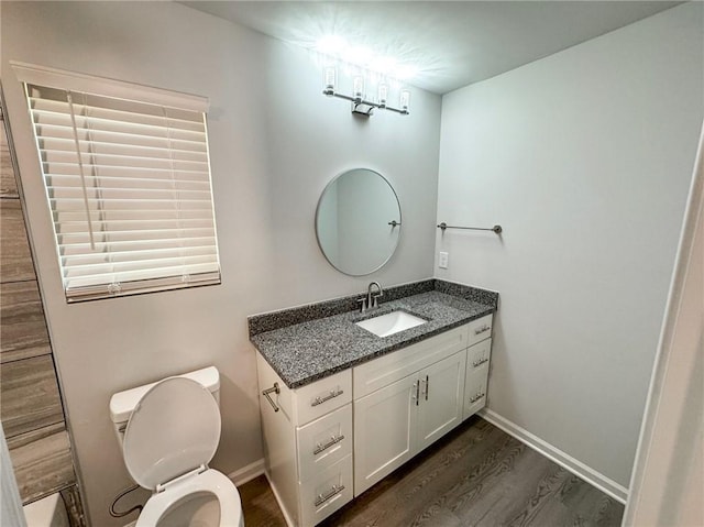 bathroom with toilet, vanity, wood finished floors, and baseboards