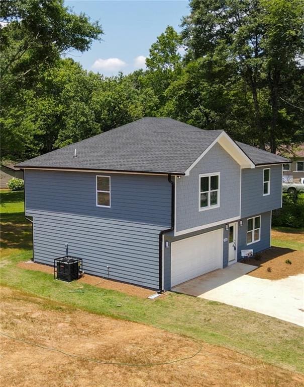 view of property exterior with roof with shingles, cooling unit, driveway, a garage, and a lawn