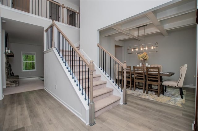 stairs with coffered ceiling, wood finished floors, a notable chandelier, and beamed ceiling