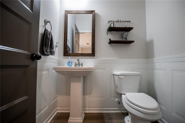 bathroom featuring wainscoting, wood finished floors, a decorative wall, toilet, and a sink