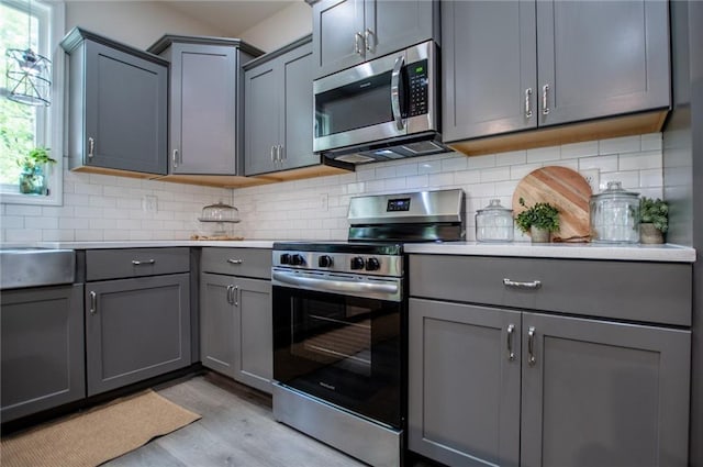 kitchen with gray cabinetry, light countertops, stainless steel appliances, and light wood finished floors