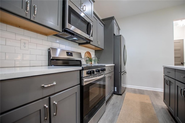 kitchen with gray cabinetry, backsplash, stainless steel appliances, and wood finished floors