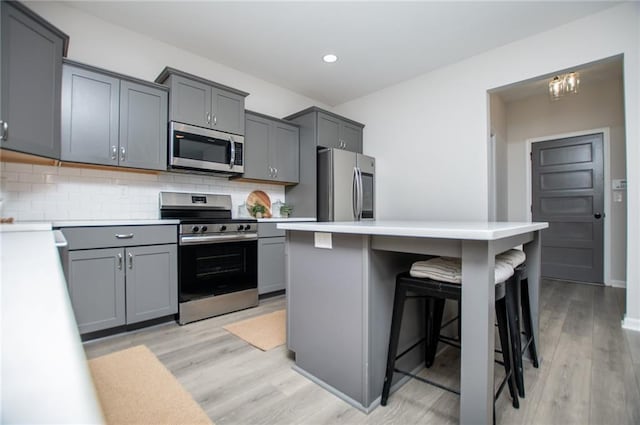 kitchen featuring a kitchen bar, tasteful backsplash, gray cabinetry, light countertops, and stainless steel appliances