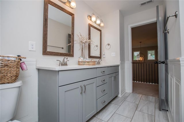 bathroom with visible vents, double vanity, toilet, a wainscoted wall, and a sink