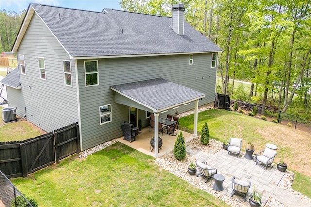 back of house with a chimney, roof with shingles, central AC unit, a patio area, and a yard