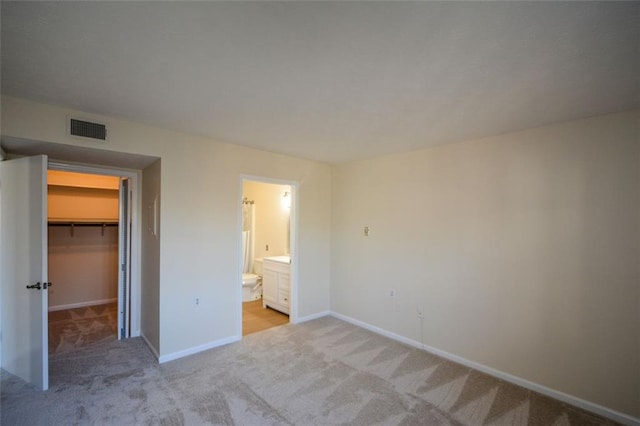 unfurnished bedroom featuring connected bathroom, light colored carpet, a spacious closet, and a closet