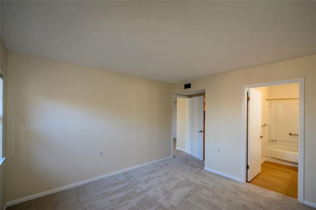 unfurnished bedroom featuring light colored carpet and ensuite bath