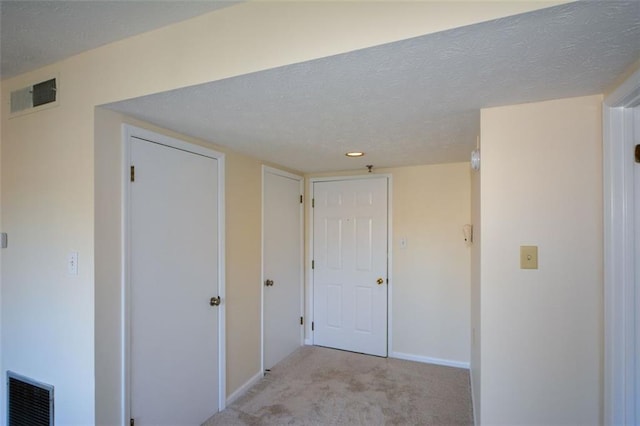 hall with a textured ceiling and light colored carpet