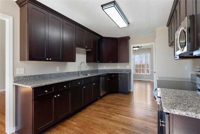 kitchen featuring appliances with stainless steel finishes, light wood-style floors, a sink, a textured ceiling, and dark brown cabinetry