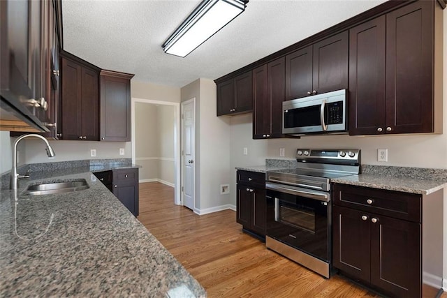 kitchen featuring dark brown cabinetry, light wood-style flooring, appliances with stainless steel finishes, and a sink