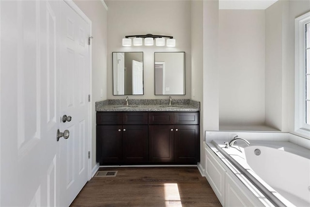 full bathroom with double vanity, a garden tub, a sink, and wood finished floors