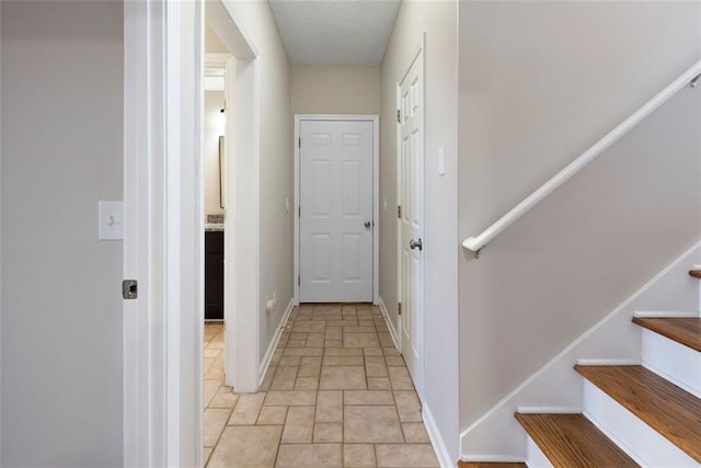 corridor with stairs, a textured ceiling, and baseboards