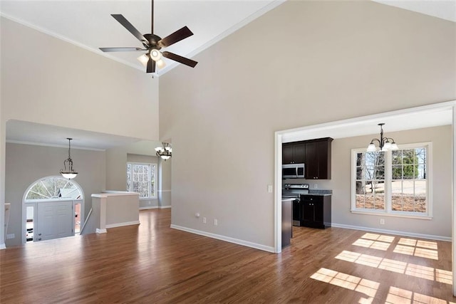 unfurnished living room with baseboards, wood finished floors, a towering ceiling, and crown molding