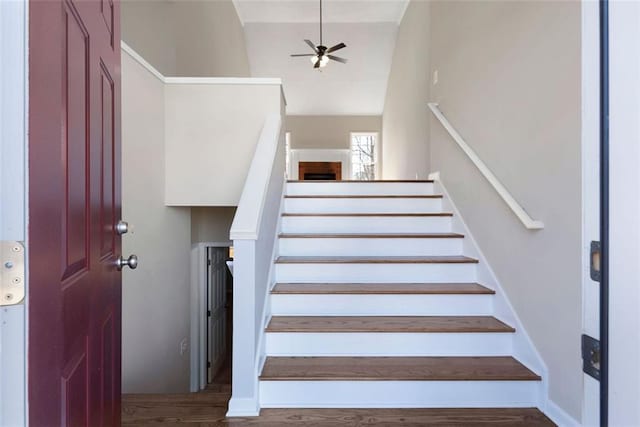 staircase with wood finished floors, a ceiling fan, and baseboards