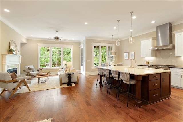 385 Windy Pines Trl, Roswell, GA 30075 - kitchen featuring wall chimney exhaust hood, crown molding, open floor plan, a breakfast bar area, and dark wood-type flooring