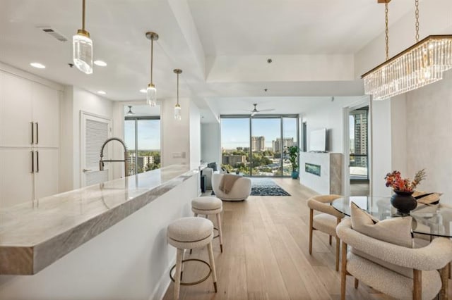 kitchen with hanging light fixtures, light stone countertops, white cabinets, light hardwood / wood-style flooring, and ceiling fan with notable chandelier