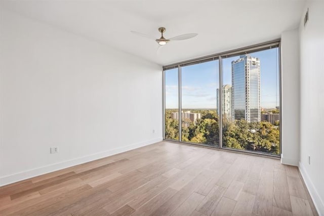 spare room with a wall of windows, ceiling fan, and light hardwood / wood-style flooring