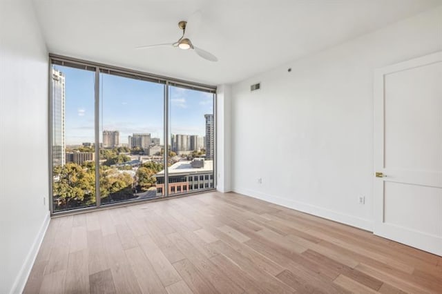 empty room featuring floor to ceiling windows, ceiling fan, and light hardwood / wood-style floors